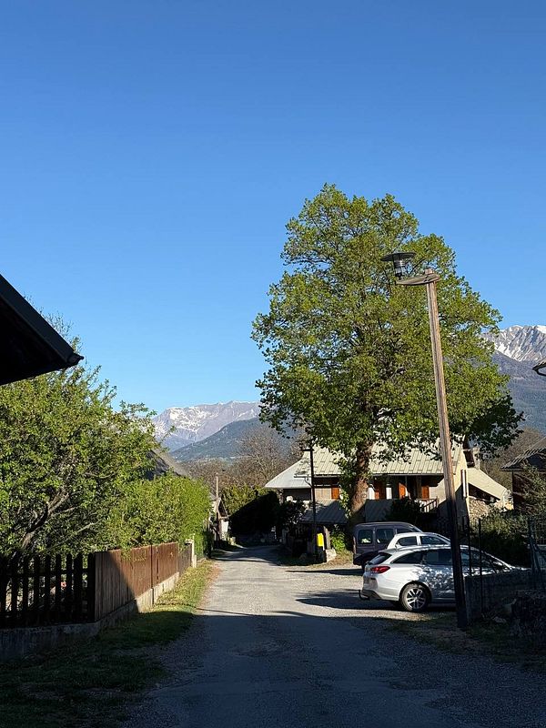 Panoramic mountain landscape with a winding road and parked motorcycles under a clear sky in Hautes-Alpes, France.