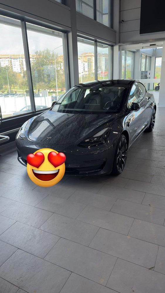 A sleek gray Tesla Model 3 is parked inside a modern showroom.