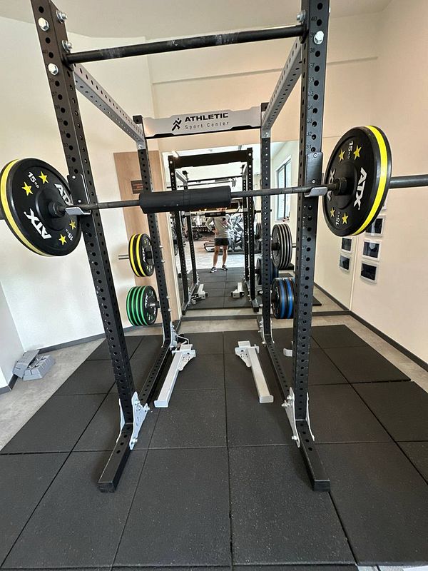 A gym setup featuring a squat rack with weights and a mirrored wall.