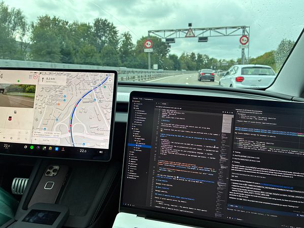 Photo of a car interior with a laptop on the passenger seat, showing coding work on the screen and a 5G hotspot device nearby.