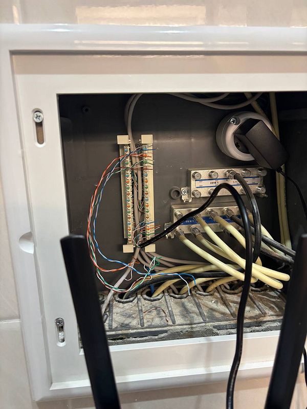 The image depicts a patch box with various Ethernet cables and connections inside a wall-mounted enclosure.