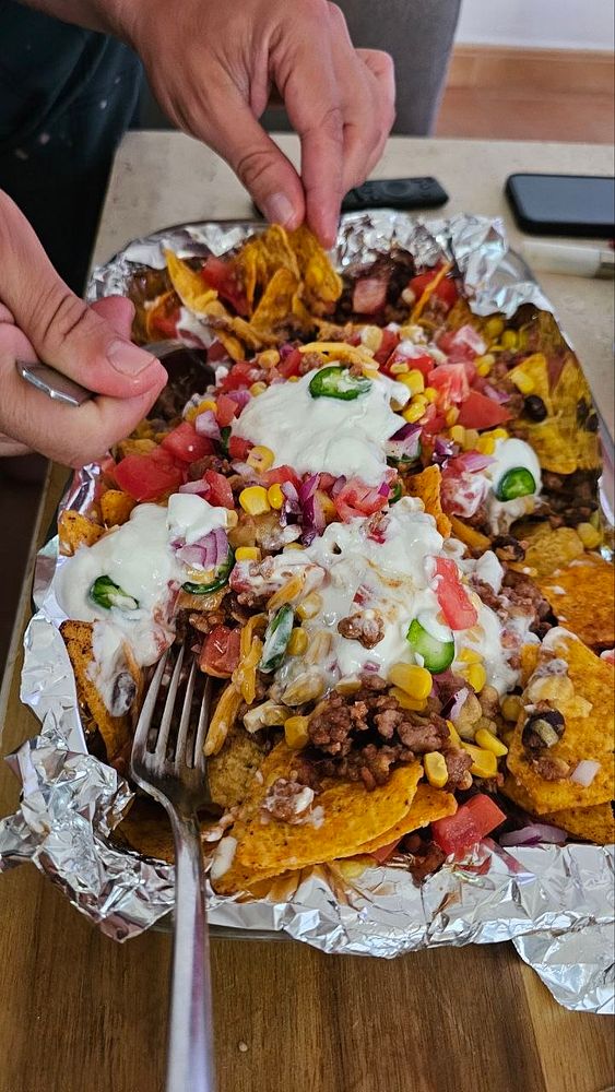 A close-up view of homemade nachos layered with ground beef, jalapeños, black olives, and melted cheese on a baking tray.