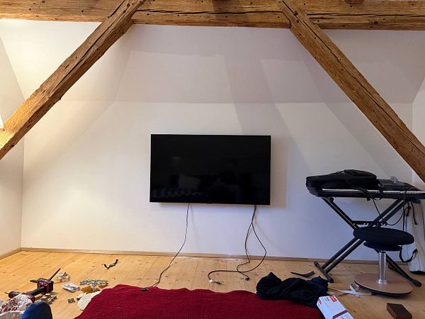 Two men working together to attach a TV to drywall using mounting tools.