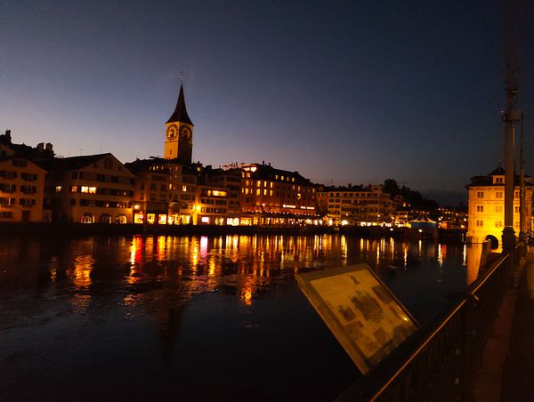 A serene nighttime view of a riverside cityscape illuminated by streetlights and reflections on the water.