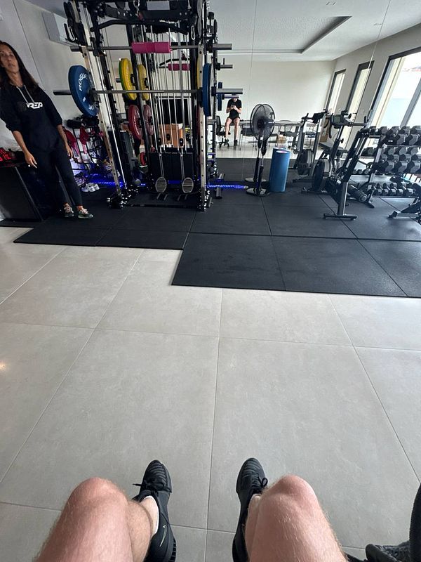 The image captures a gym interior with workout equipment and individuals engaged in fitness activities.