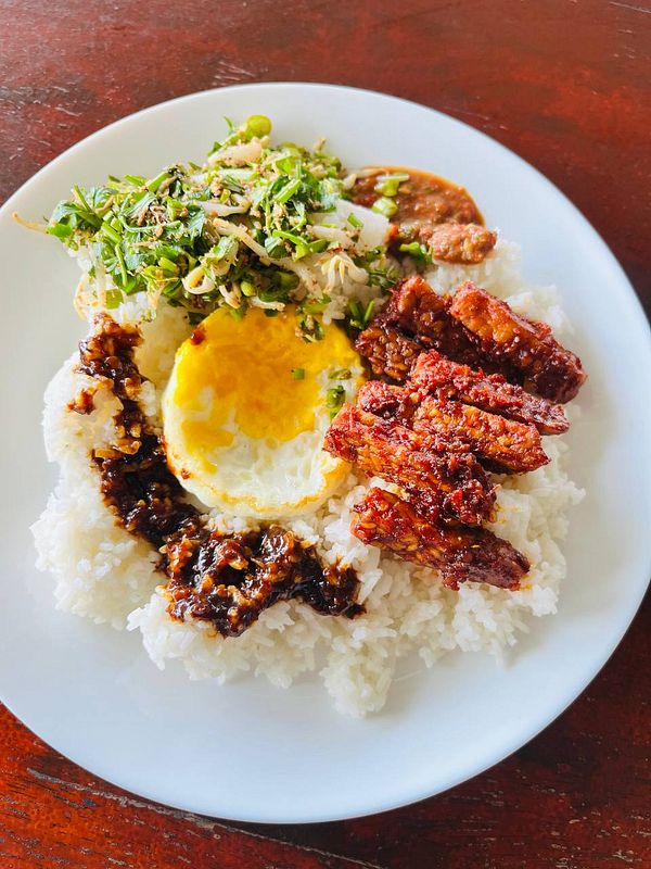 A plate of rice topped with various accompaniments including fried egg, meat, and vegetables.
