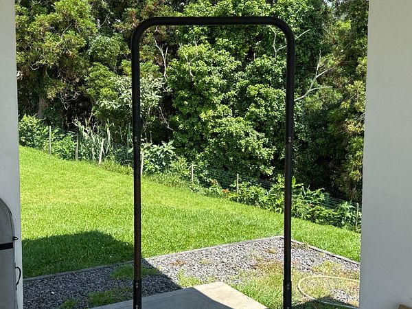 A pull-up bar is set up outdoors in a grassy area surrounded by trees.