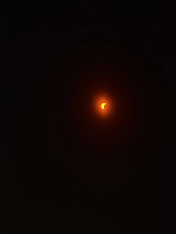 Night sky with a solar eclipse and stars scattered above a silhouetted mountain range.