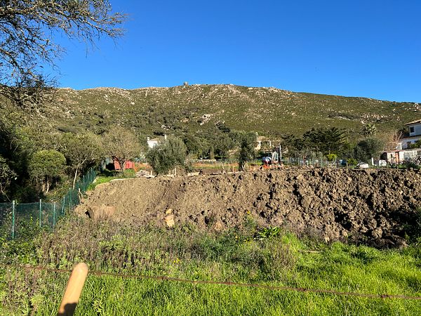 A construction site with a large dirt mound and a mountainous backdrop.