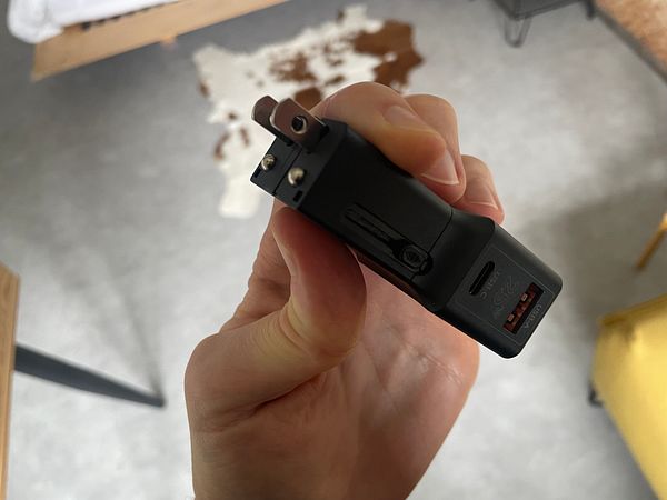 A compact mobile charger designed for international use is being held in a person's hand.