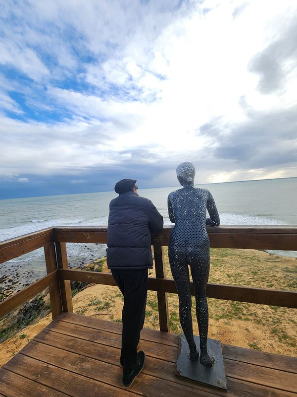 A person stands next to a metallic sculpture overlooking the sea.