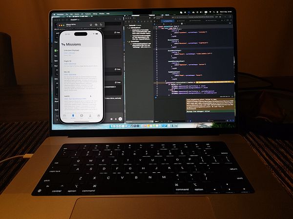 A laptop screen displays a mobile app interface alongside coding software.
