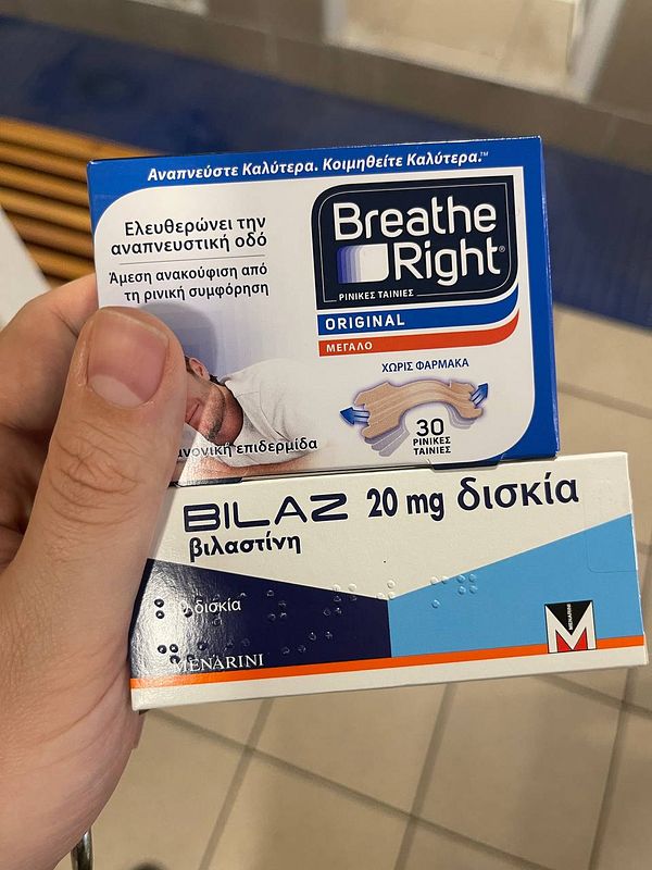 A person is holding two allergy-related products: Breathe Right nasal strips and Bilaz antihistamine tablets.