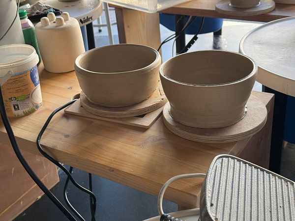 A cozy pottery studio scene with a person shaping clay on a potter's wheel and various ceramic items displayed.