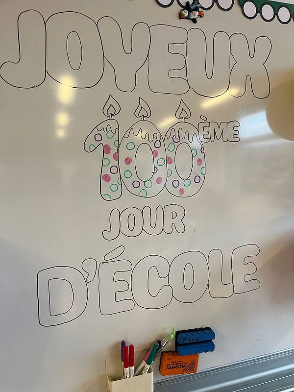 A whiteboard displays a colorful celebration of the 100th day of school.