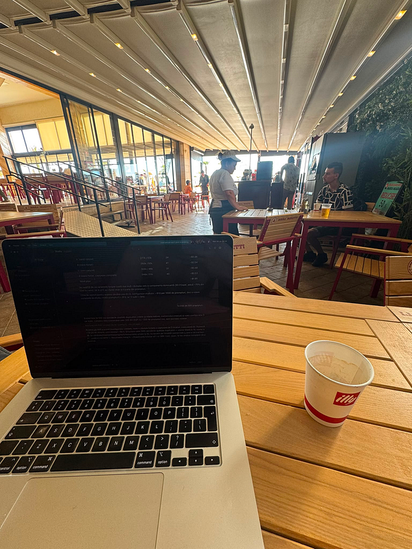 A photo of a woman intently working on her laptop at a wooden table in a cozy, warmly lit cafe setting.