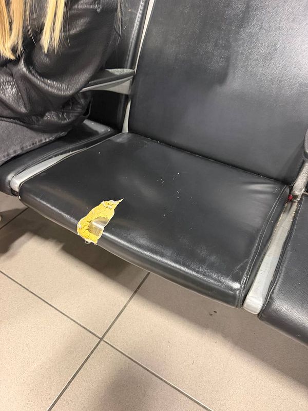 Black airport waiting seats with a torn seat cushion revealing yellow foam underneath.