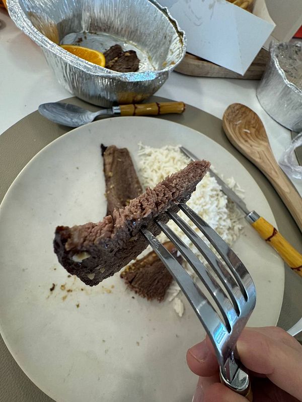 A fork holds a piece of well-cooked picanha meat above a plate of rice.