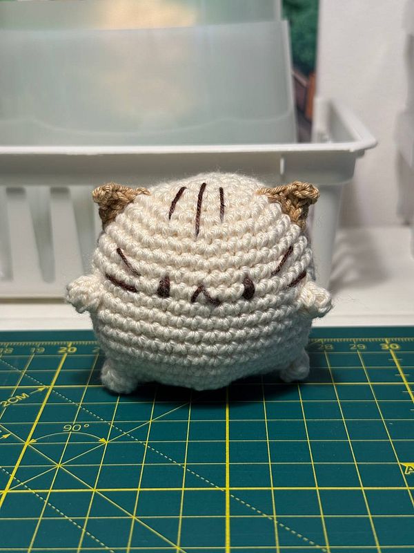 A crocheted critter resembling a cute, round cat with small ears and a friendly expression.