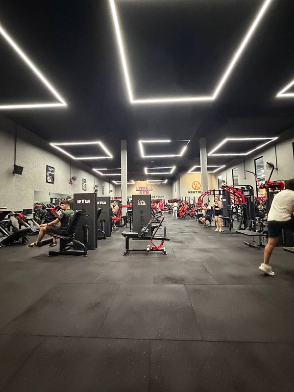 A photo of a man working out at a gym on a rowing machine with personal trainer assistance.
