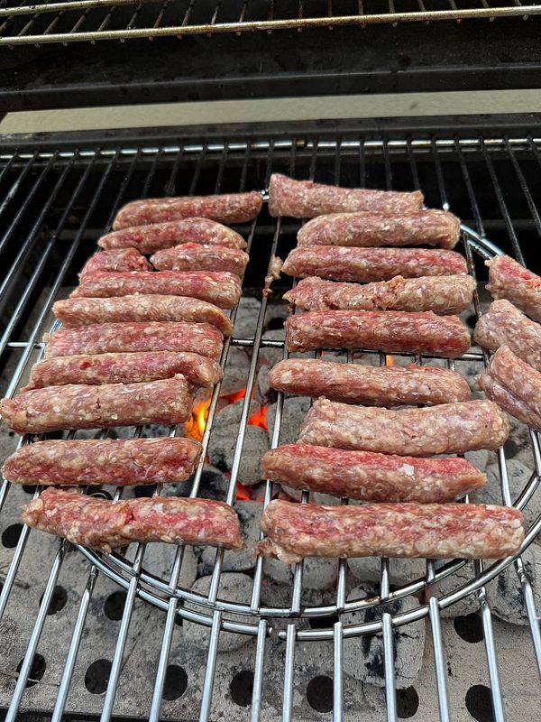 Grilled sausages are arranged on a barbecue grill over glowing coals.