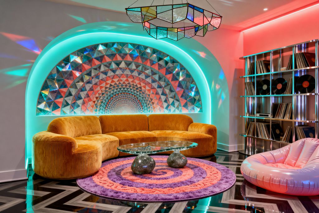A psychedelic living room centers on a plush mustard velvet curved sectional set before an arched alcove lined with triangular iridescent mosaic tiles, haloed by neon teal backlighting and reflected by a multicolor stained-glass pendant. A round purple-and-coral spiral shag rug anchors a glass coffee table with two polished stone bases, while a pink inflatable lounge and a stainless-steel record shelf loaded with vinyls sit on a glossy black-and-gray chevron floor under pink and teal ambient lighting.