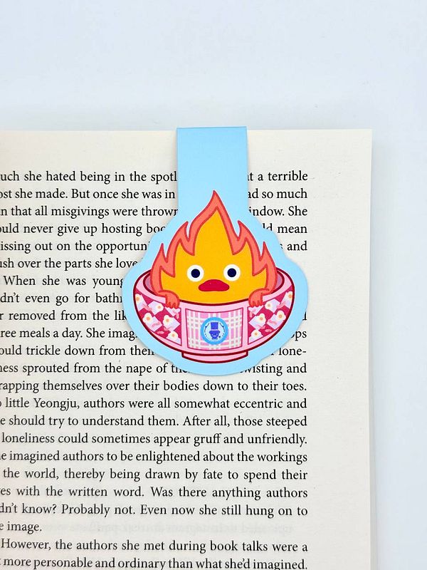 A colorful magnetic bookmark featuring a cartoon flame character is placed on an open book page.