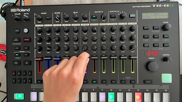 A close-up view of a Roland TR-8S drum machine with a hand adjusting the controls.
