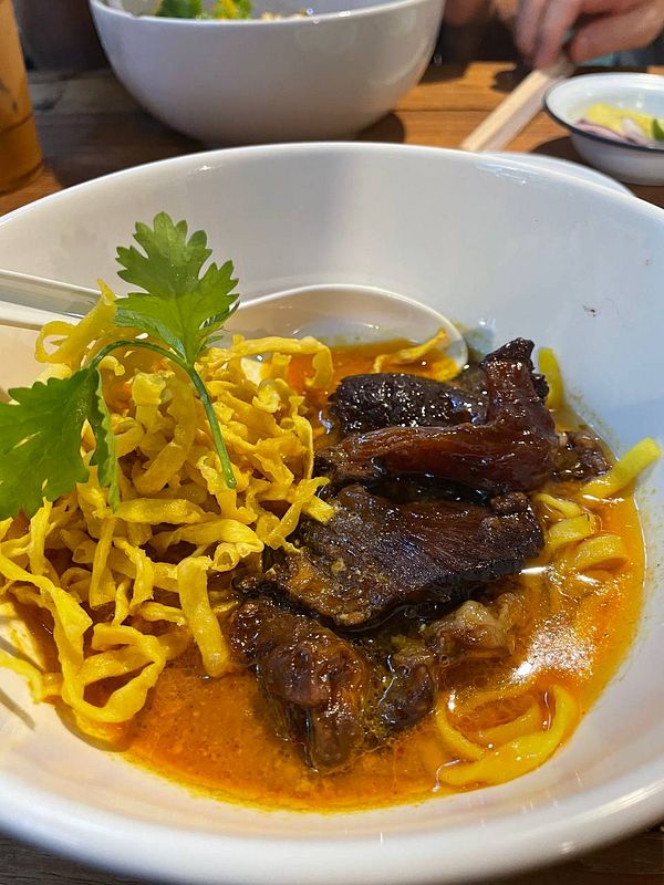 A bowl of Kao Soy, a northern Thai dish, featuring noodles, meat, and garnishes.
