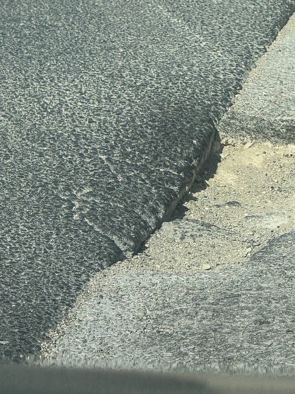A large, dangerous hole in the road is visible, showcasing significant wear and damage to the asphalt.