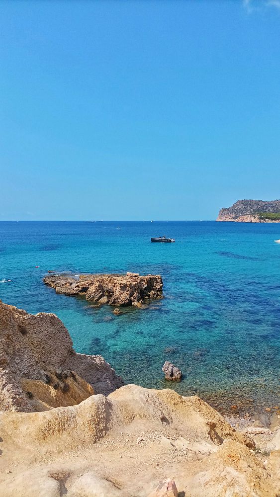 A scenic view of a clear blue ocean with rocky formations and a boat in the distance.