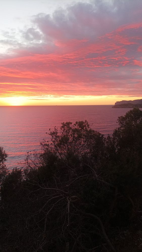 Sunset over a calm sea with silhouetted people and a boat, framed by a rock outcrop.