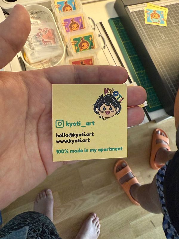 A hand holds a colorful business card featuring the brand 'Kyoti' and contact information.