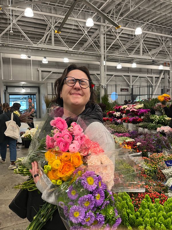 A person is joyfully holding a large bouquet of colorful flowers in a vibrant flower market.