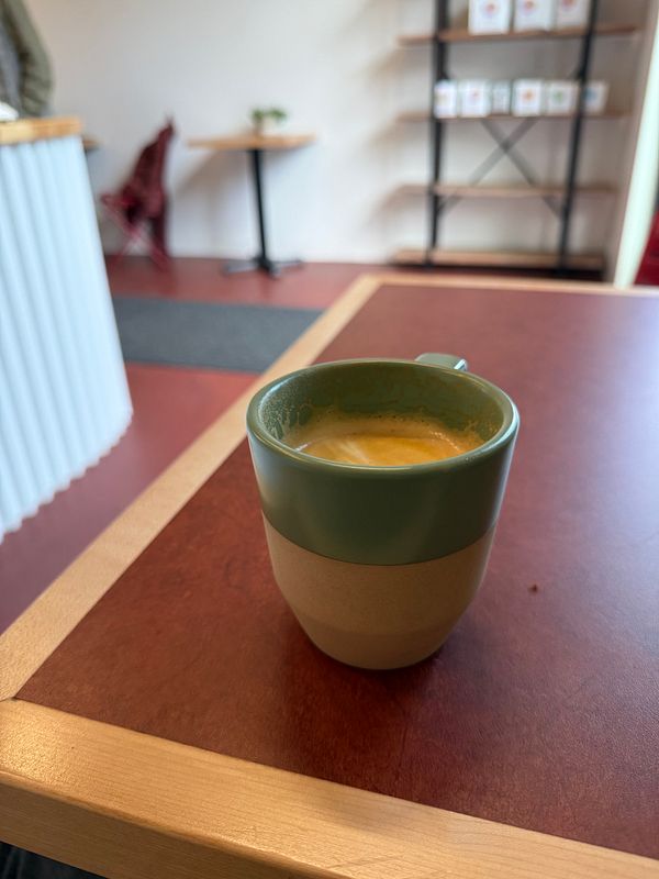 A flat white coffee is placed on a wooden table in a cozy café setting.