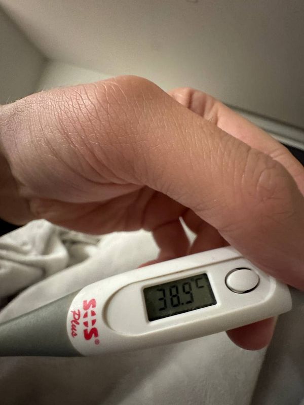A hand holding a digital thermometer displaying a temperature reading of 38.9°C.