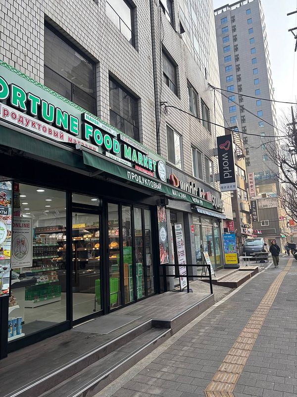 A street scene in a Soviet-style neighborhood in Seoul featuring buildings with Cyrillic signage and a busy pedestrian area.