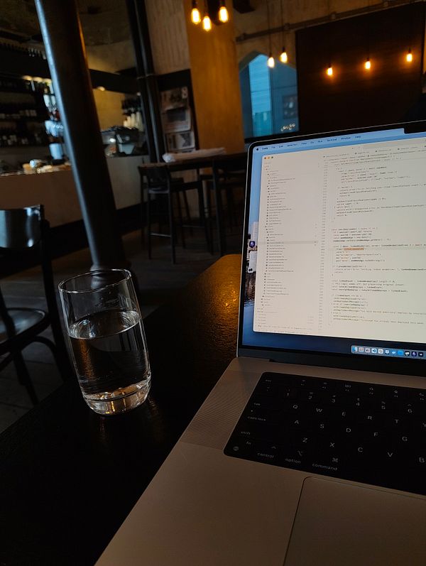 A laptop displaying code is positioned on a table in a cozy café setting.