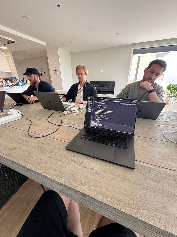 A group of three individuals is working collaboratively at a table with laptops in a modern coworking space.