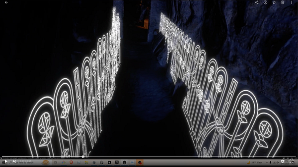 A narrow, illuminated pathway featuring intricate line art along the walls, set in a dark, cavernous environment.