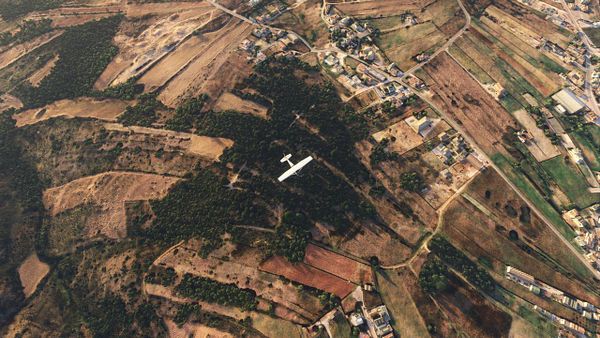 An aerial view of a landscape with a small aircraft flying over fields and a village.