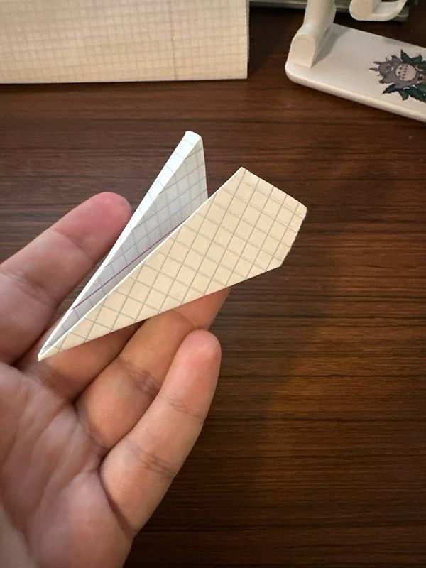A hand holds a small paper airplane made from grid-patterned paper.