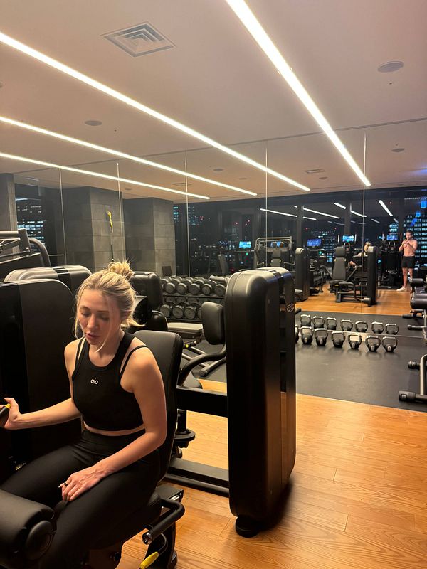 A woman is exercising in a modern gym with various workout equipment in the background.