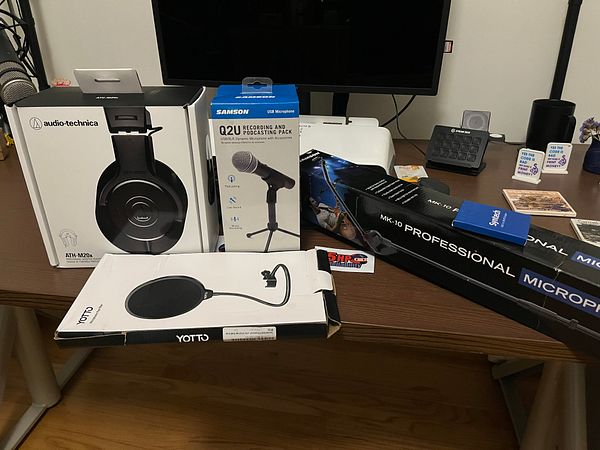 An organized collection of varied audio recording and podcasting equipment arranged on a wooden table.