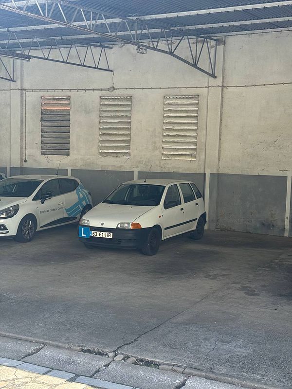 A white car with a learner's plate is parked in a garage next to another vehicle.