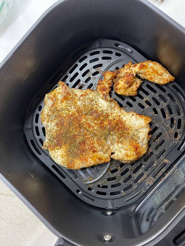 A seasoned chicken breast is placed in an air fryer basket.