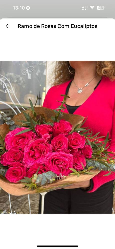 A woman holds a vibrant bouquet of pink roses with eucalyptus in a flower shop.