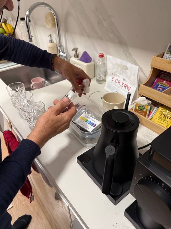 A person is preparing to test a water sample using a testing kit in a kitchen setting.