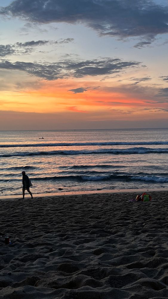 A serene beach scene at sunset with a person walking along the shore.