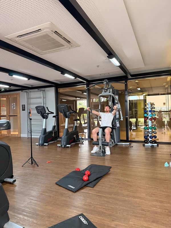 A gym setup with fitness equipment and a video screen showing a remote personal trainer session.